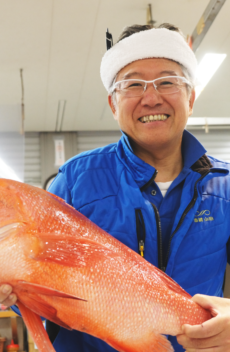 立派な魚を抱えて笑顔を見せる仲卸スタッフ