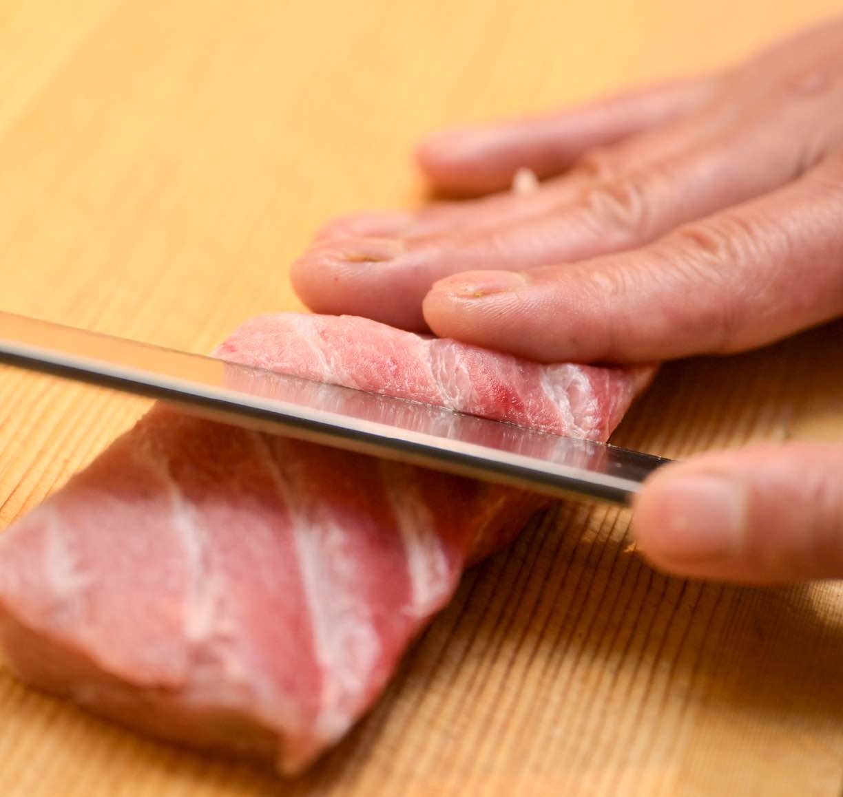本鮪の大トロのサクに丁寧に包丁を入れる職人の手元