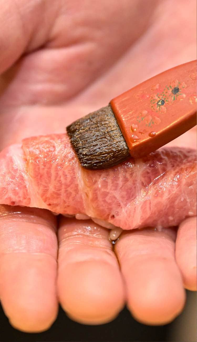 本鮪の握り寿司に刷毛で煮切り醤油を塗る職人の手元