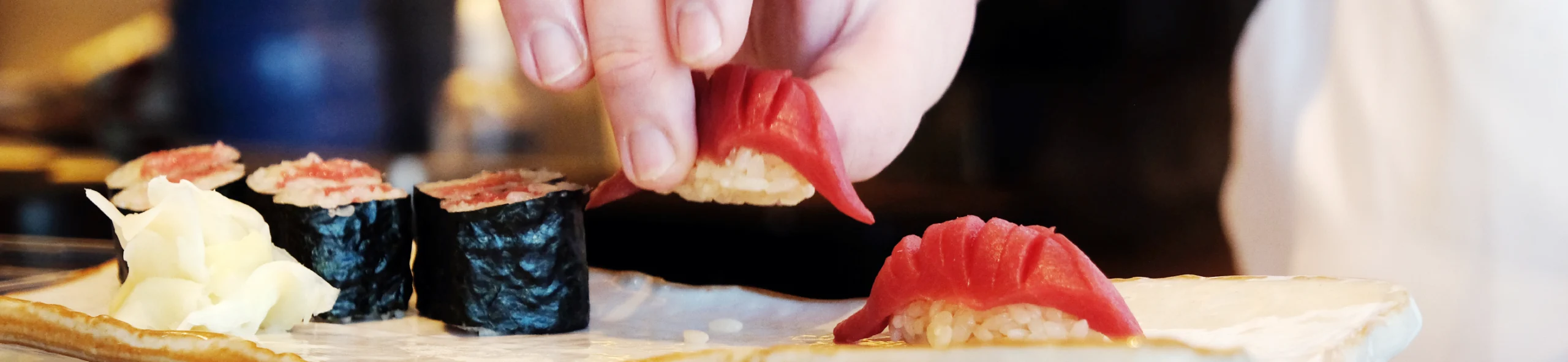 切り込みが入った赤身の握り寿司をつまむ手と、皿に並ぶ寿司