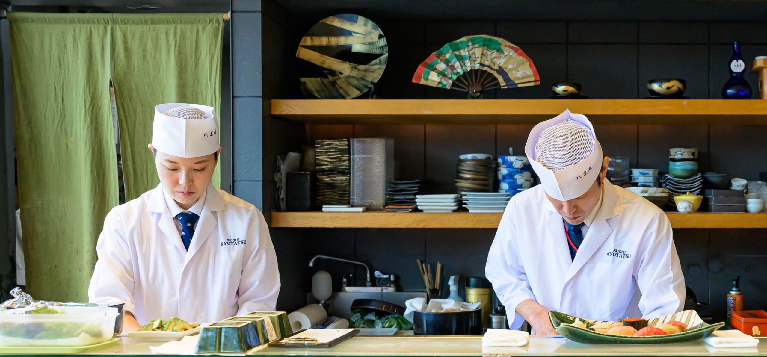 カウンター内で調理する板前と壁に掛かったメニュー木札