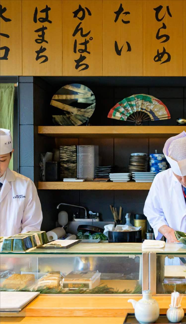 カウンター内で調理する板前と壁に掛かったメニュー木札