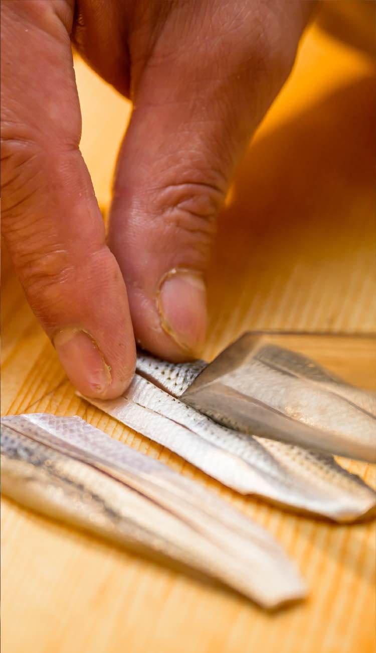 光り物の魚に丁寧に包丁を入れる仕込みの様子